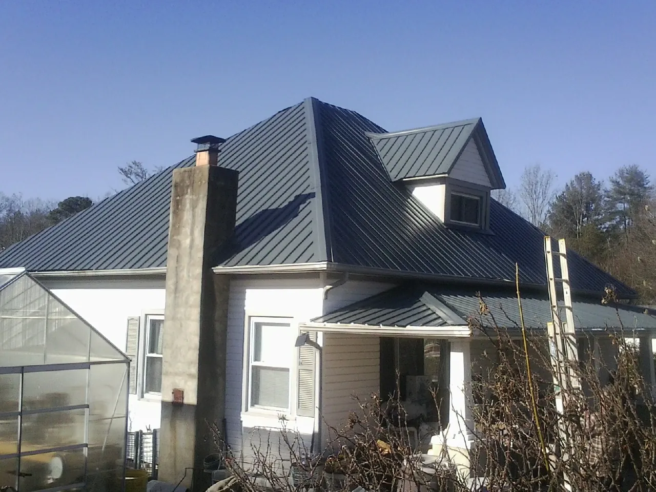 Dark blue standing seam metal roof on a white farmhouse with dormer — Slate & Tile Roof Repair by Roofing Brothers in Deferiet