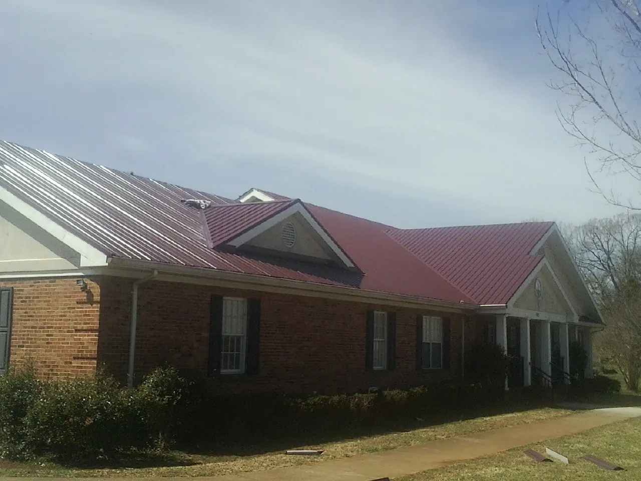 Red metal roof with gabled entries on a long brick building, from a Hail Damage Roof Repair job in Deferiet