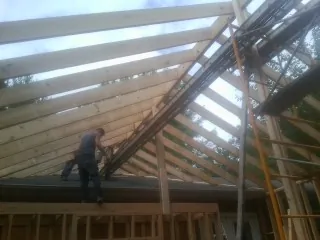 Rafters going up over a new addition with a worker on the wall in Deferiet