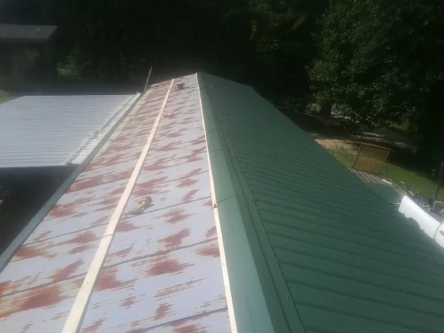 Old rusted panels beside newly installed green metal roofing — Wind Damage Roof Repair by Roofing Brothers in Deferiet