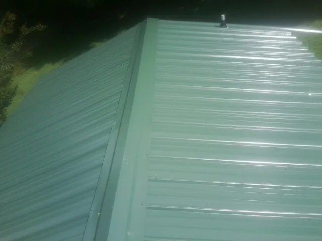 New green metal panels meeting at the ridge of a roof — Flat Roof Repair work by our crew in Deferiet