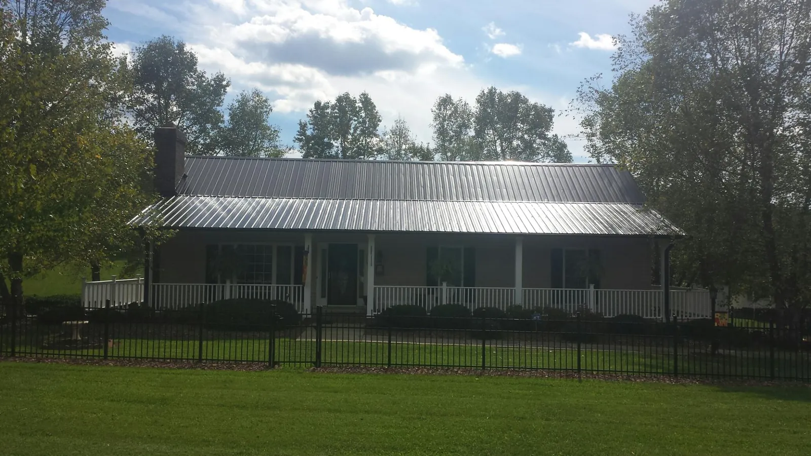 Gray metal roof on a brick ranch with a full width front porch — Gutter Guard Installation work by our crew in Deferiet
