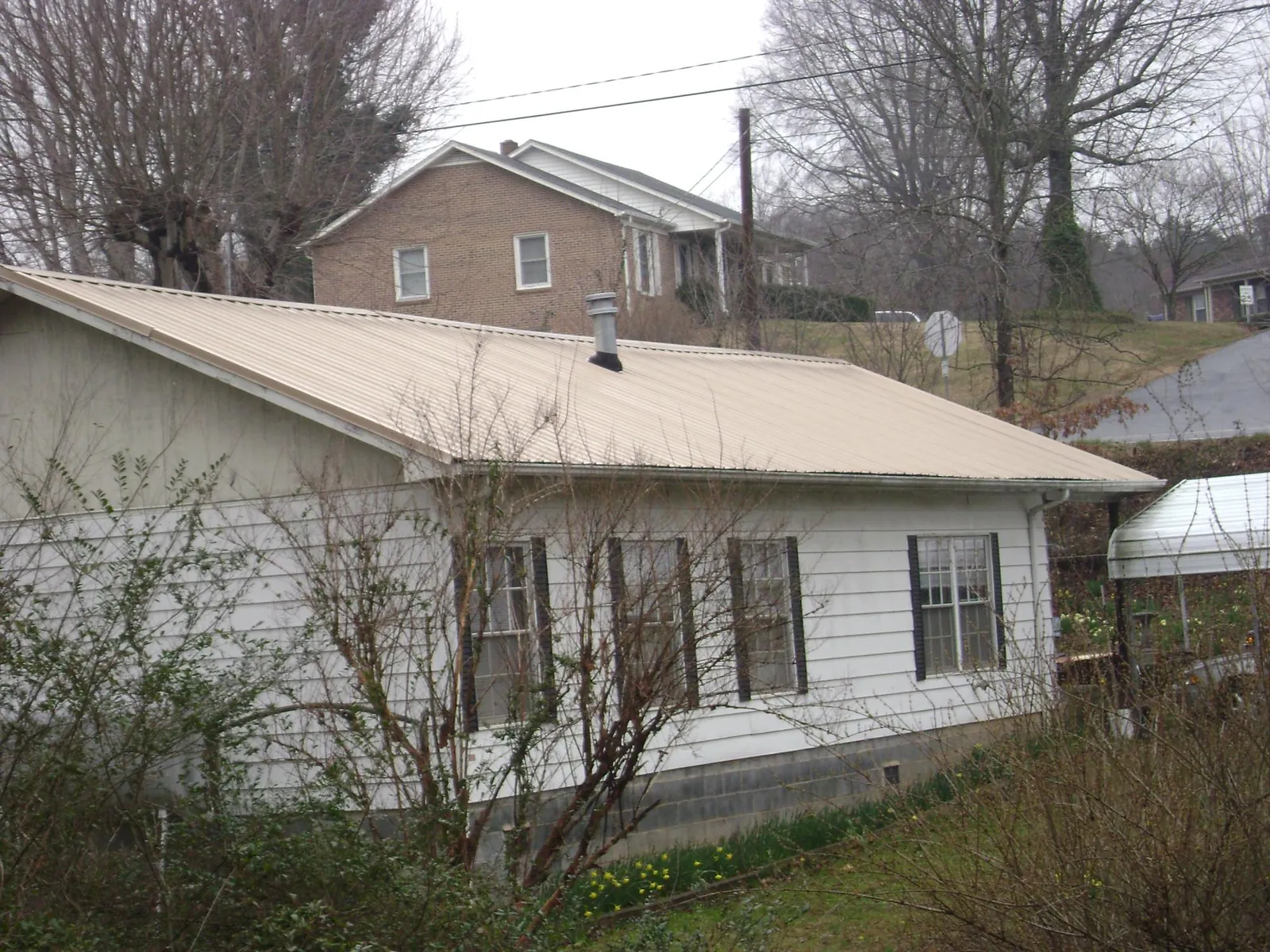 Tan metal roof on a white sided house set into a hillside — Commercial Roofing by Roofing Brothers in Deferiet